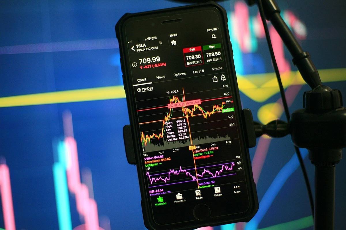 Smartphone affichant graphiques financiers sur trépied, écran lumineux, arrière-plan flou coloré