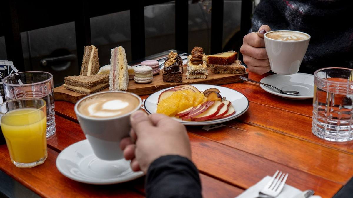 Deux mains tenant des tasses de café sur une table avec des tartines, des verres d'orange et d'eau Deux mains tenant des tasses de café sur une table avec des tartines, des verres d'orange et d'eau