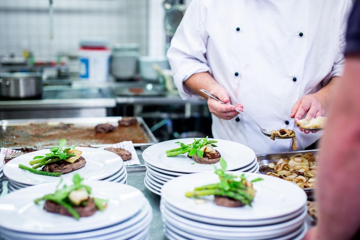 Chef pr&eacute;parant des assiettes de steak avec des l&eacute;gumes verts