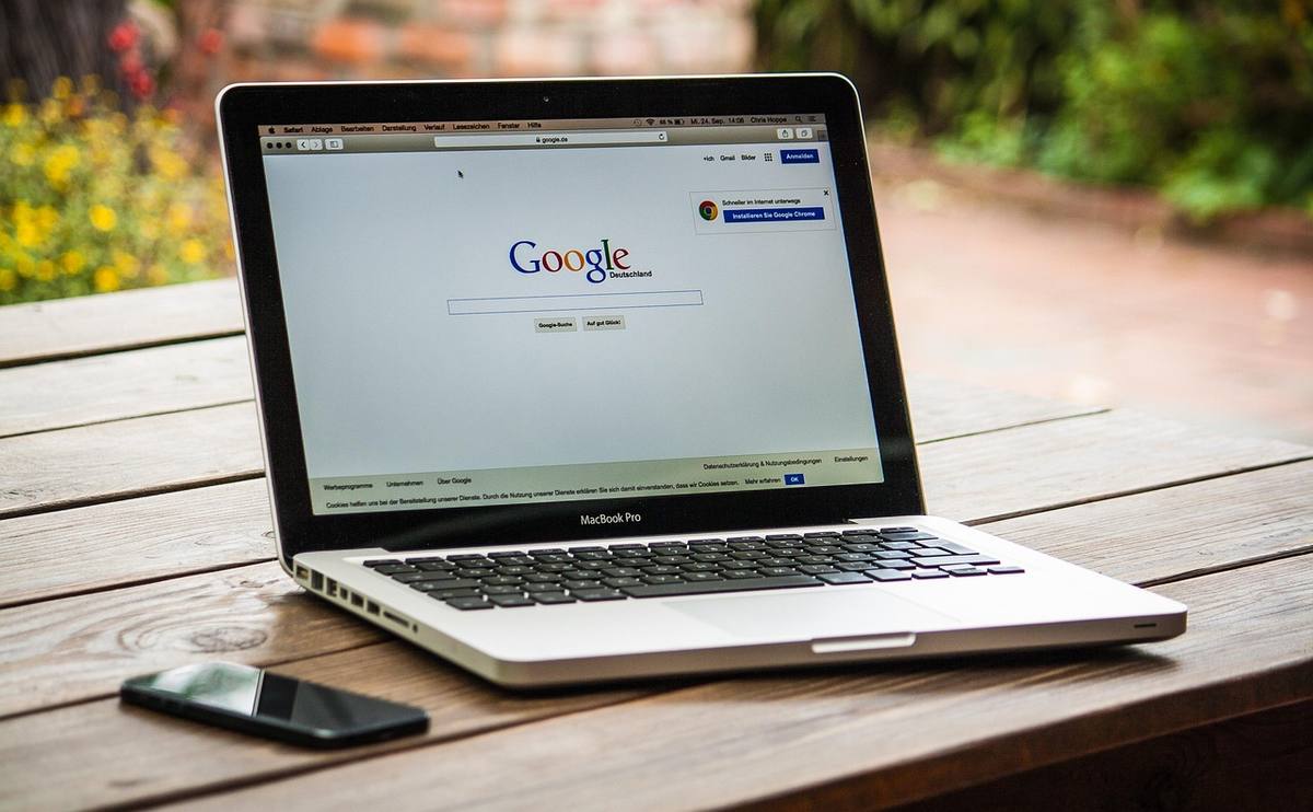 Laptop ouvert affichant la page Google, posé sur table en bois extérieure