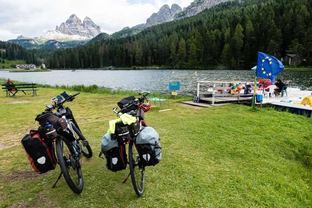 Deux vélos de voyage avec sacoches stationnés au bord d'un lac de montagne avec camping
