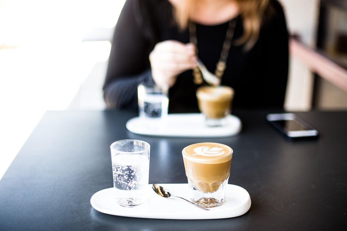 Femme à table noire avec café latte, verre d'eau et téléphone près d'elle