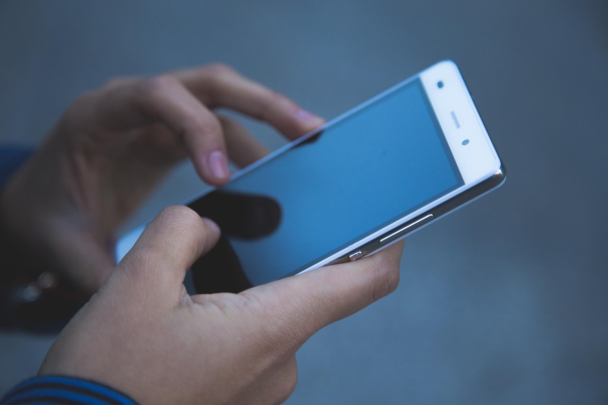 Main tenant un smartphone blanc affichant un écran bleu sur fond gris Main tenant un smartphone blanc affichant un écran bleu sur fond gris