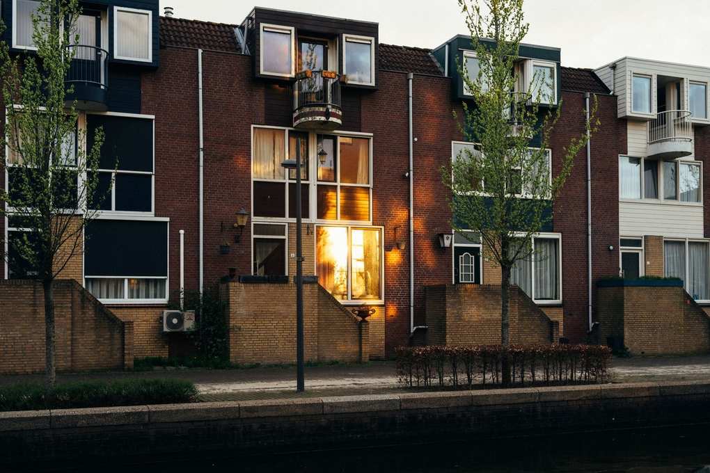 Bâtiment rouge avec fenêtres lumineuses et balcon, devant un trottoir Bâtiment rouge avec fenêtres lumineuses et balcon, devant un trottoir