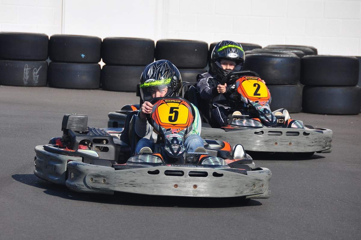 Trois jeunes pilotes en kart portant casques sur une piste couverte avec pneus de sécurité