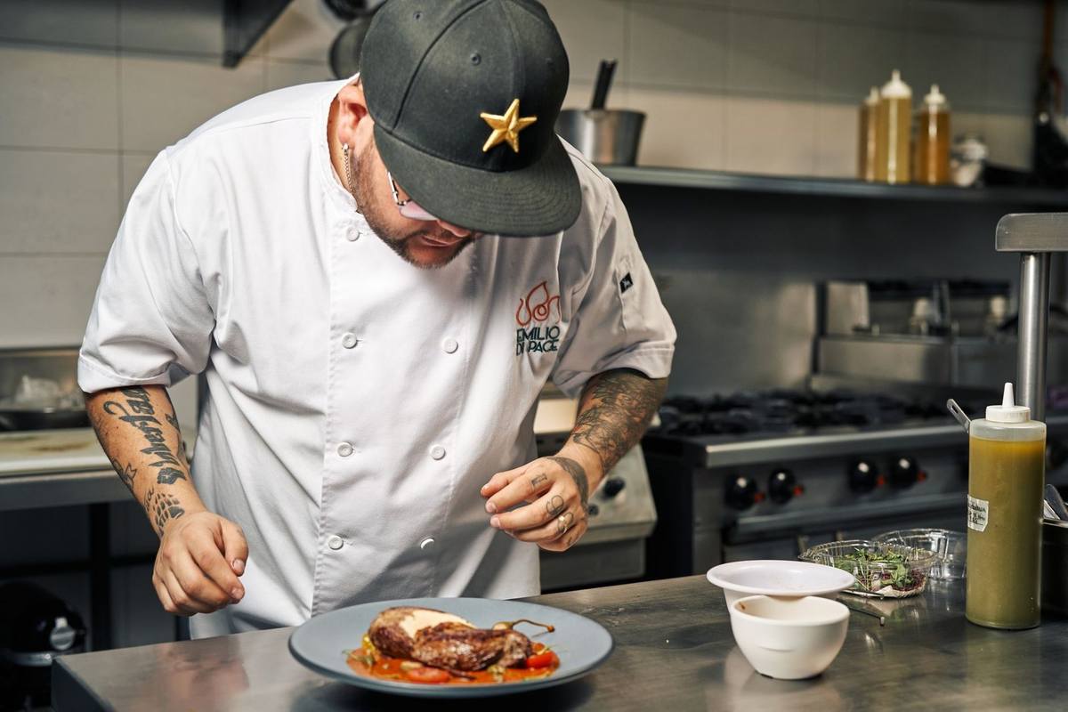 Chef tatoué examine un plat de viande dans une cuisine professionnelle