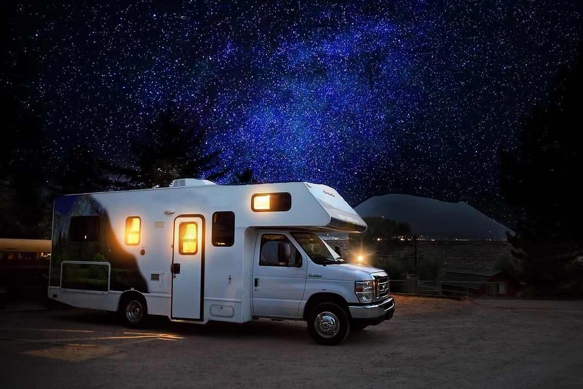 Camping-car blanc stationné de nuit avec intérieur éclairé, ciel étoilé en arrière-plan