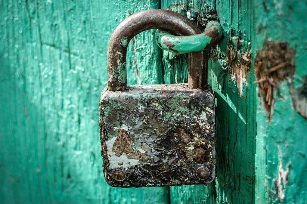 Cadenas ancien et rouillé fixé sur une porte verte décrépite et usée Cadenas ancien et rouillé fixé sur une porte verte décrépite et usée