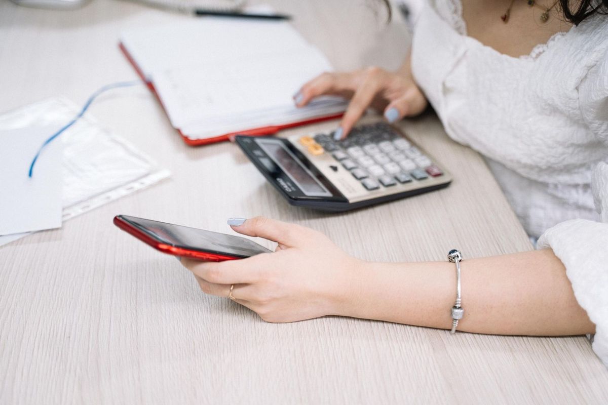 Femme manipulant un smartphone et une calculatrice sur une table de bureau Femme manipulant un smartphone et une calculatrice sur une table de bureau