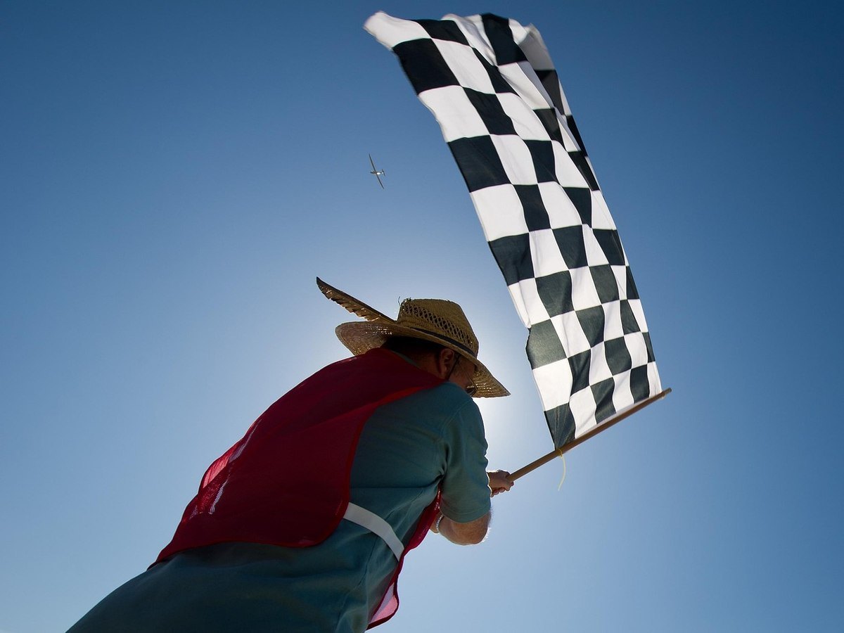 Personne levant un drapeau à damier sous un ciel bleu