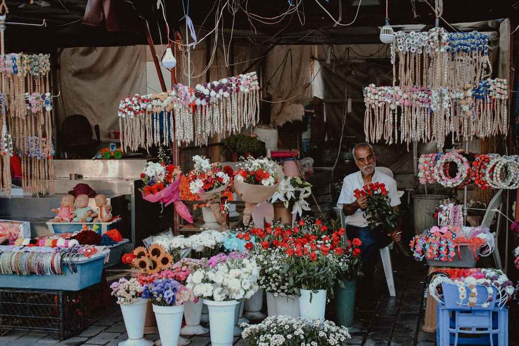 Marché fleuri avec pots, guirlandes et paniers, vendeur assis Marché fleuri avec pots, guirlandes et paniers, vendeur assis