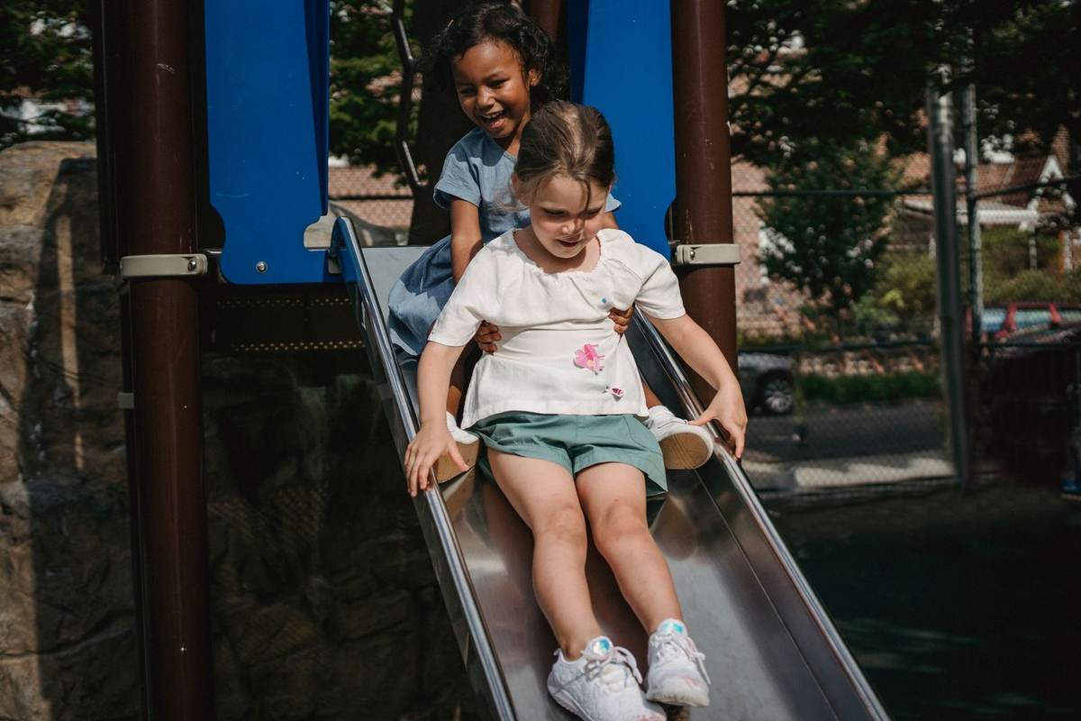 Enfants sur une glissière dans un parc, structures bleues et végétation environnante