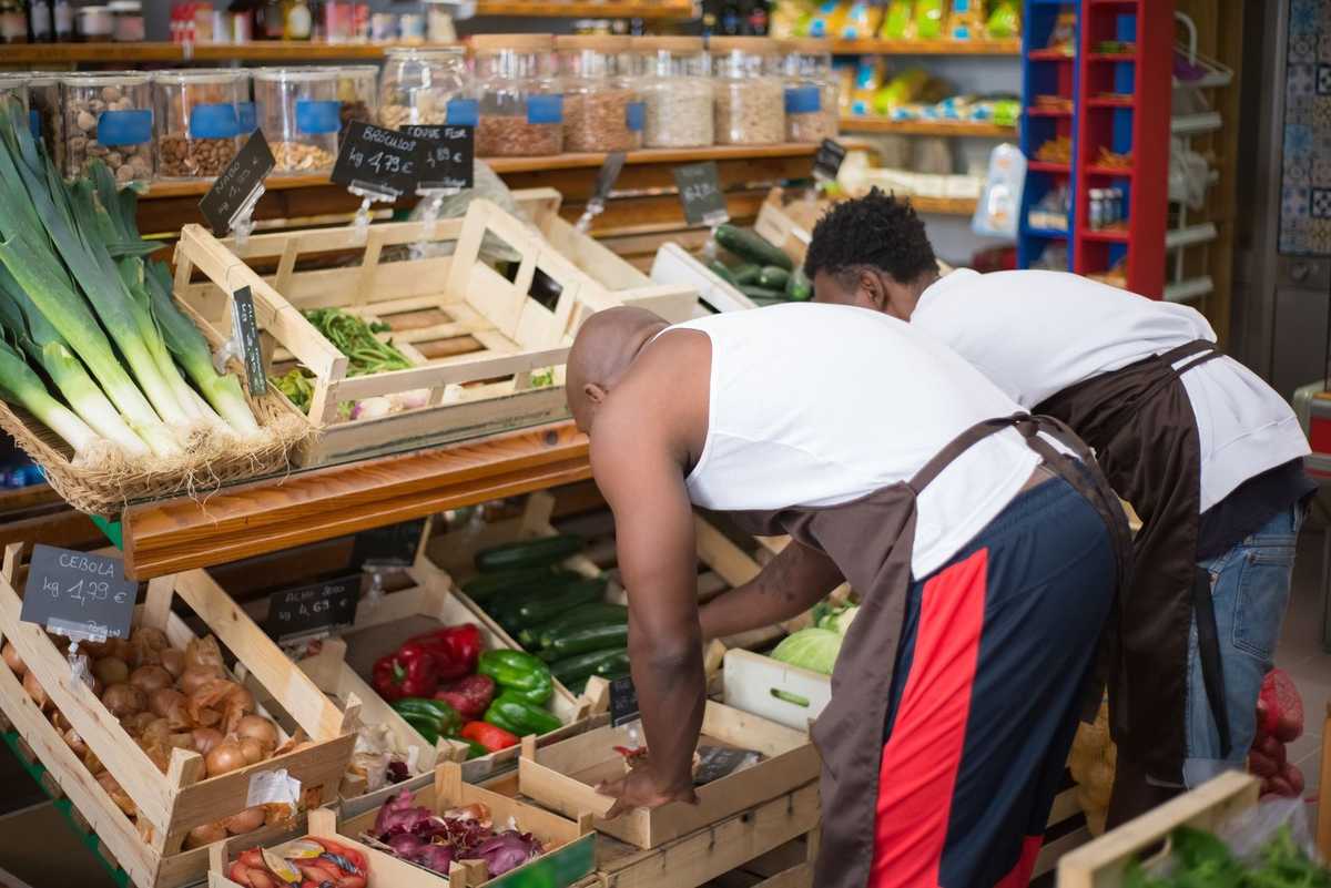 Homme en blouse blanche et tablier, manipulant des légumes dans un magasin Homme en blouse blanche et tablier, manipulant des légumes dans un magasin