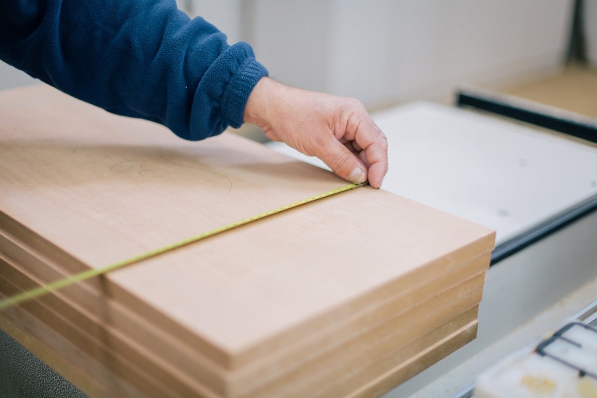 Main d'une personne mesurant des planches de bois empilées avec un mètre ruban