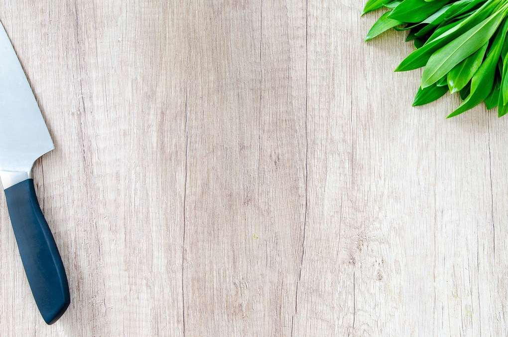 Couteau à lame argentée et poignée noire, feuilles vertes sur bois clair Couteau à lame argentée et poignée noire, feuilles vertes sur bois clair