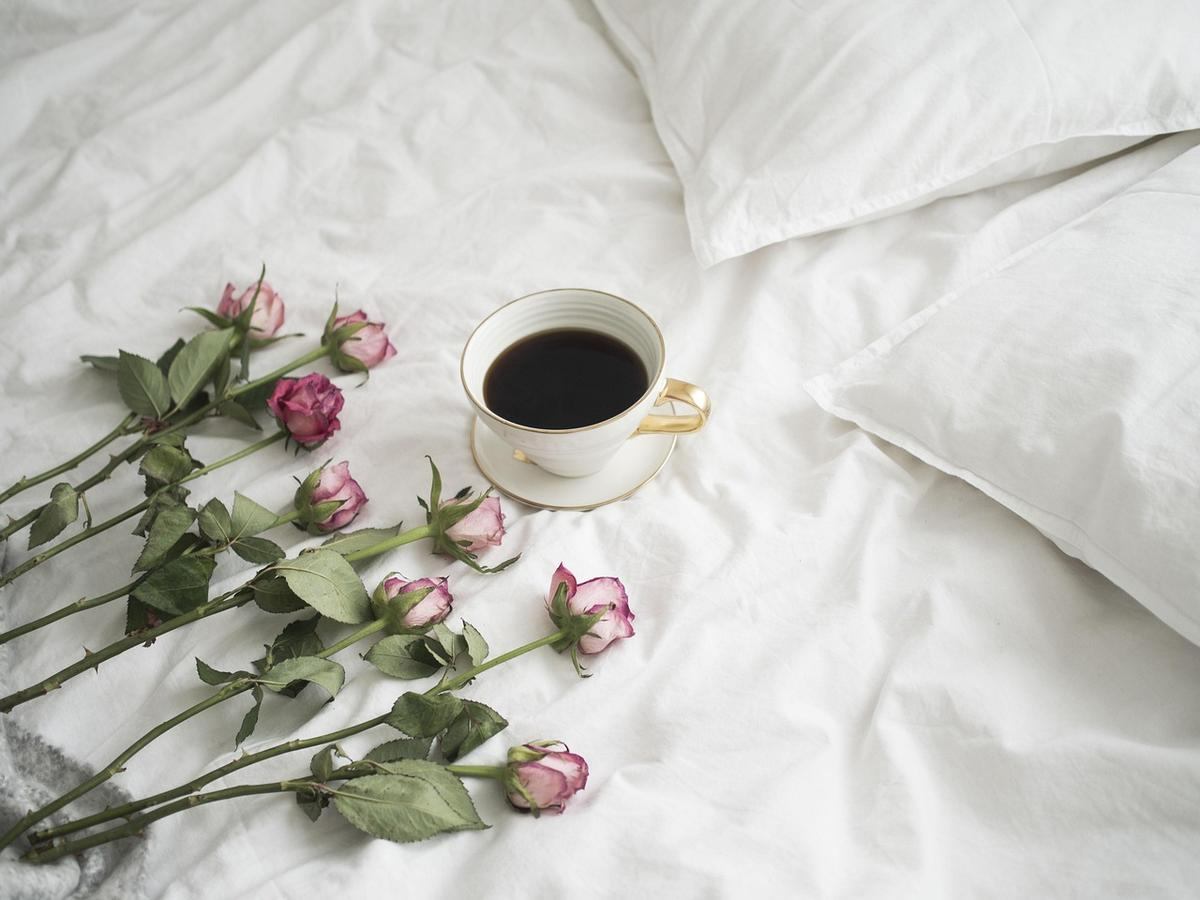 Tasse de café sur lit avec roses fanées et oreillers blancs Tasse de café sur lit avec roses fanées et oreillers blancs