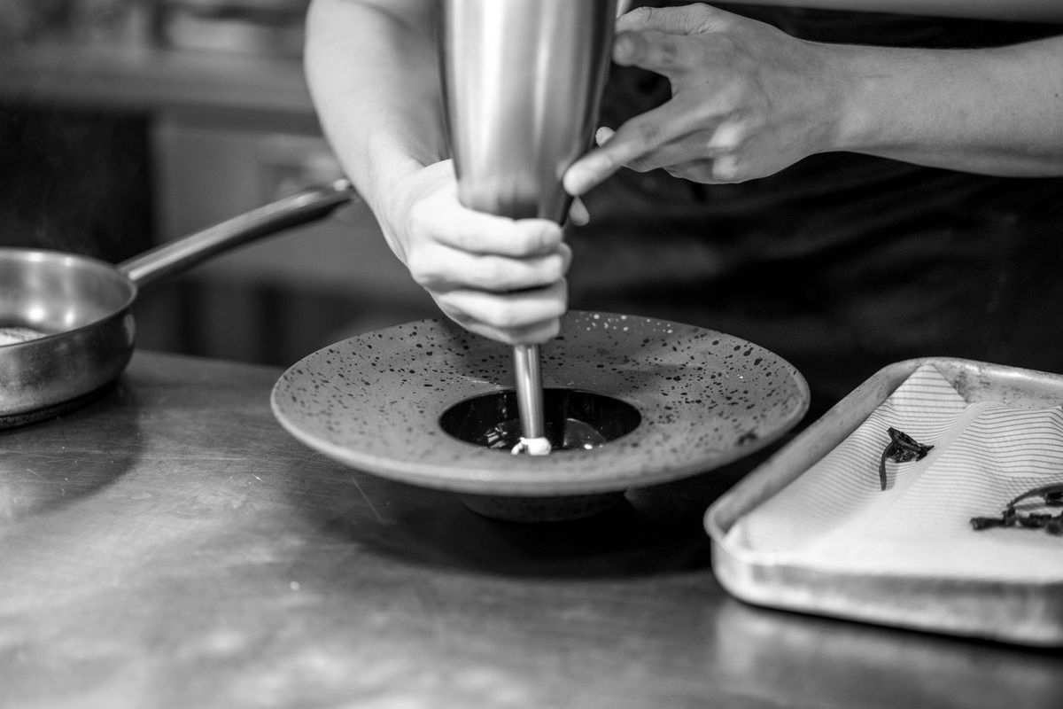 Une personne bat un mélange dans un bol avec un fouet, sur une table, près d'un plat et d'un plat à fourrure