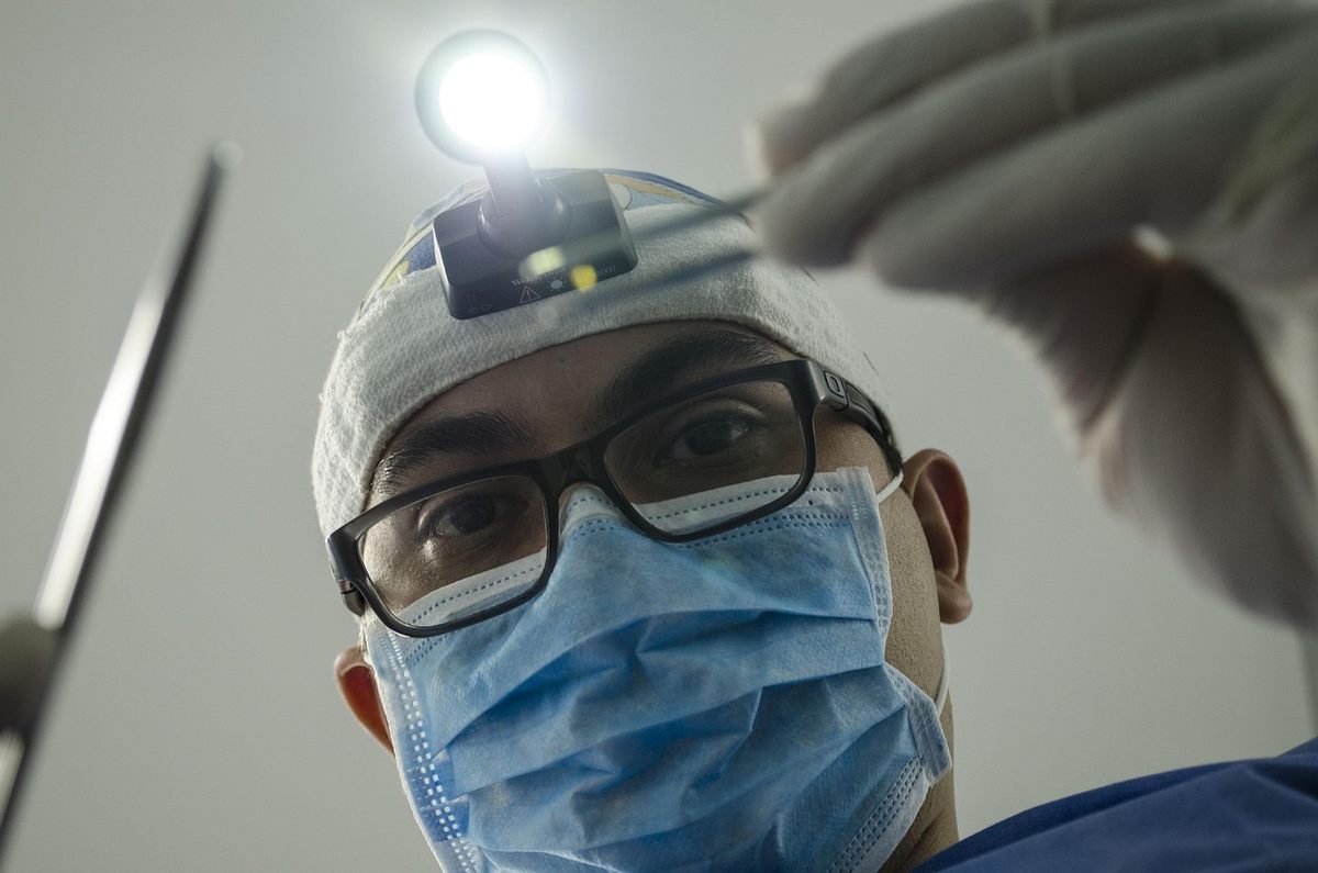 Dentiste portant masque chirurgical, lunettes et lampe frontale, prêt à intervenir
