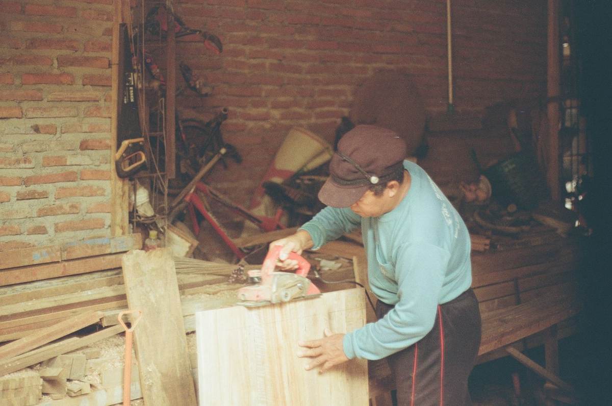 Homme ponçant une planche dans un atelier de menuiserie, outils et bois autour Homme ponçant une planche dans un atelier de menuiserie, outils et bois autour
