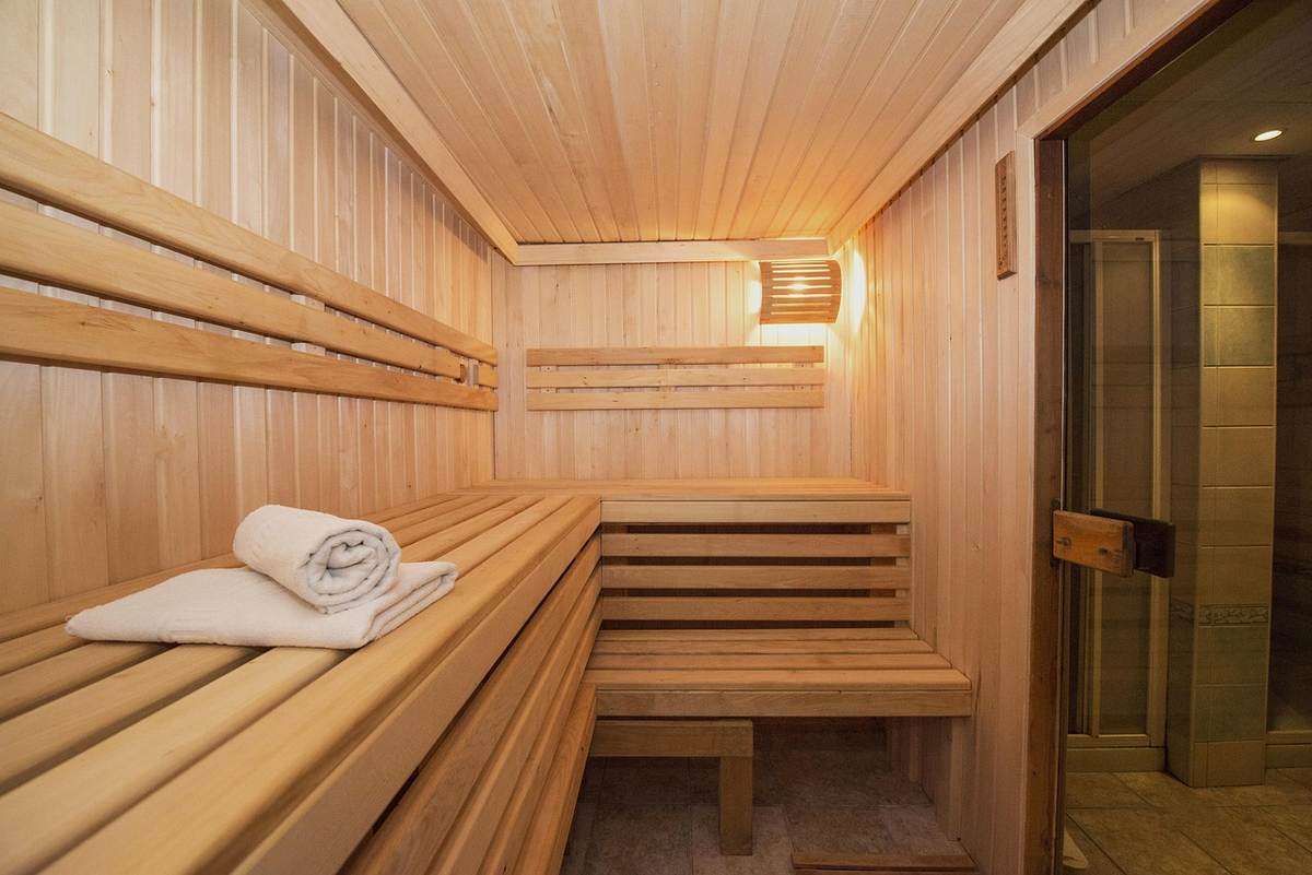 Sauna en bois avec banquettes étagées, serviette blanche et porte vitrée Sauna en bois avec banquettes étagées, serviette blanche et porte vitrée