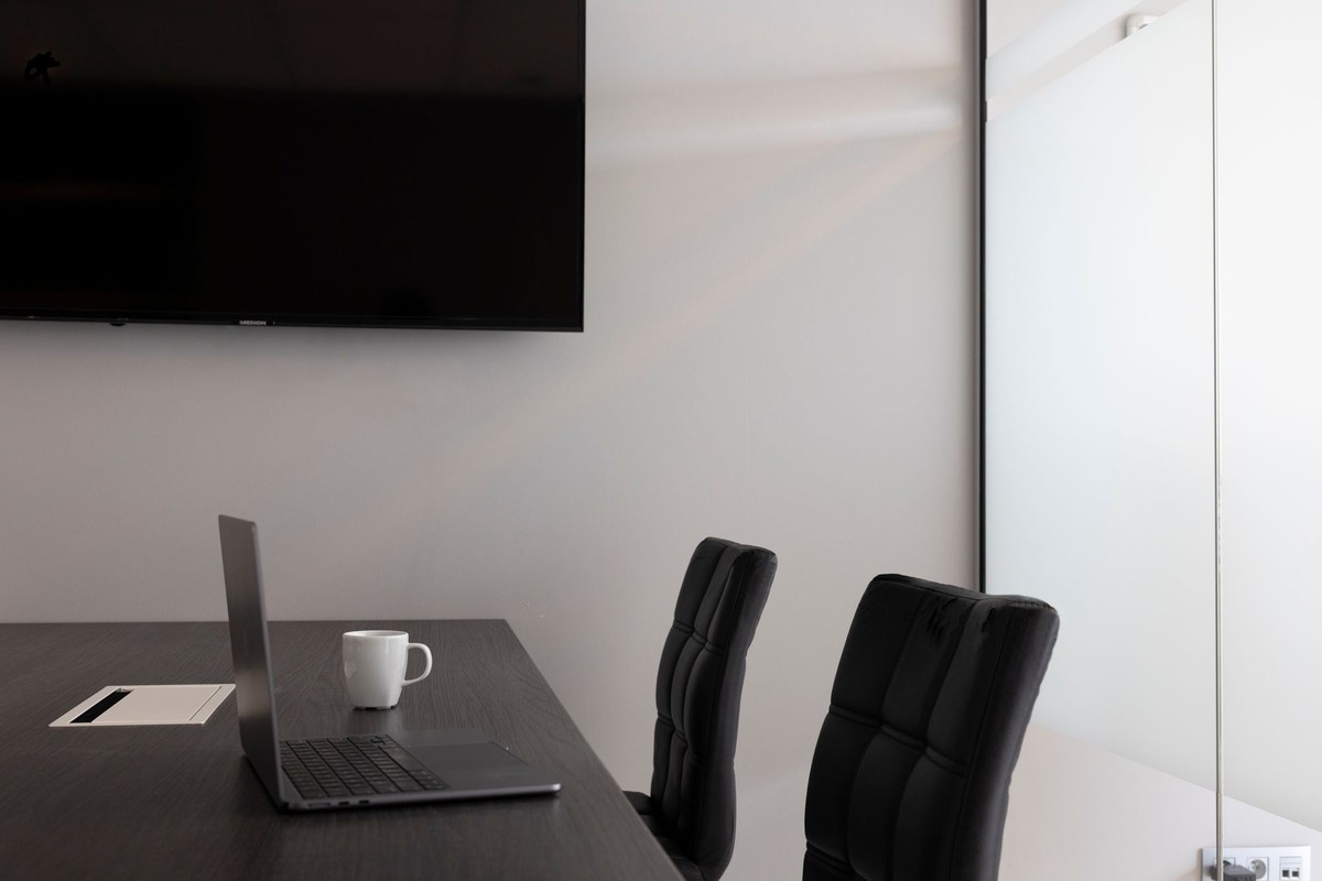 Bureau avec laptop ouvert, tasse blanche, deux chaises noires, écran mural, porte blanche Bureau avec laptop ouvert, tasse blanche, deux chaises noires, écran mural, porte blanche