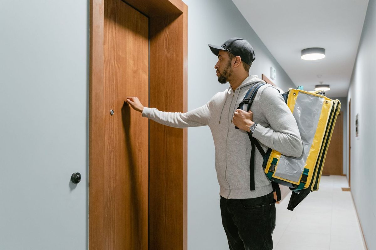 Homme portant un sac à dos jaune et gris dans un couloir, devant une porte Homme portant un sac à dos jaune et gris dans un couloir, devant une porte