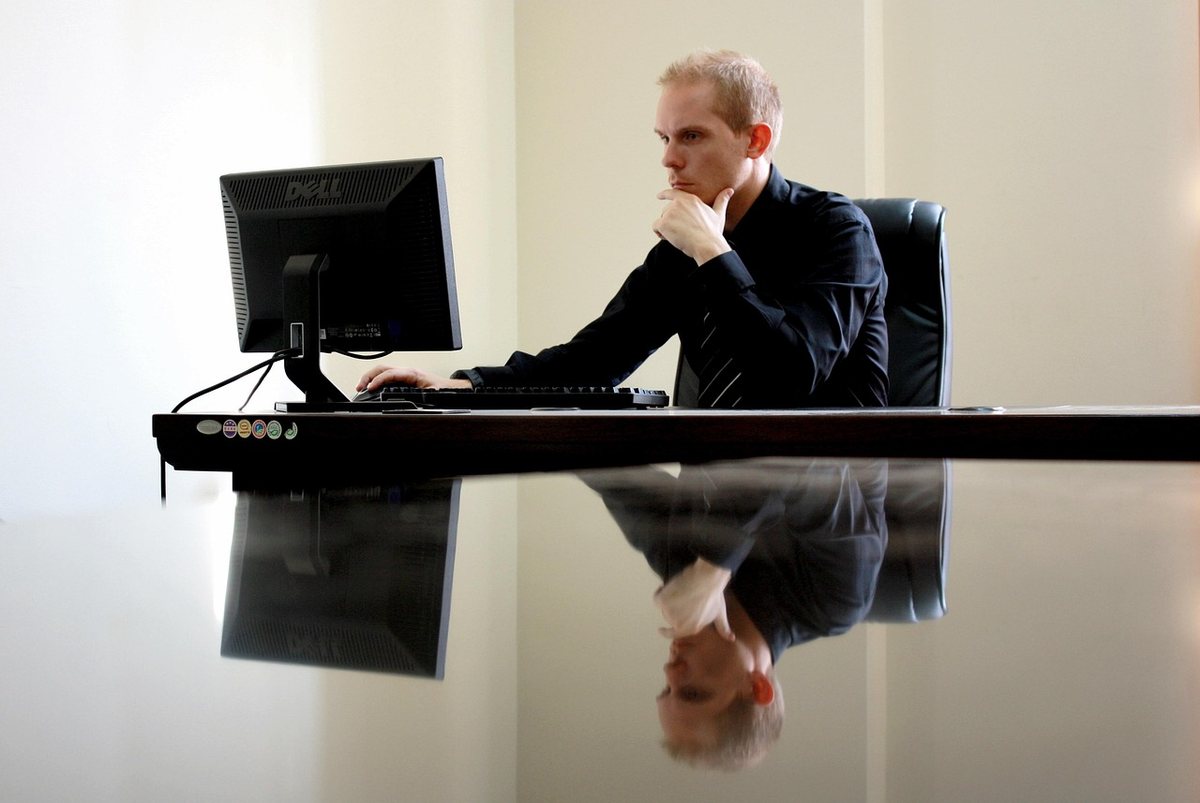 Un homme en costume travaille à son bureau face à un écran d'ordinateur dans un cadre professionnel Un homme en costume travaille à son bureau face à un écran d'ordinateur dans un cadre professionnel