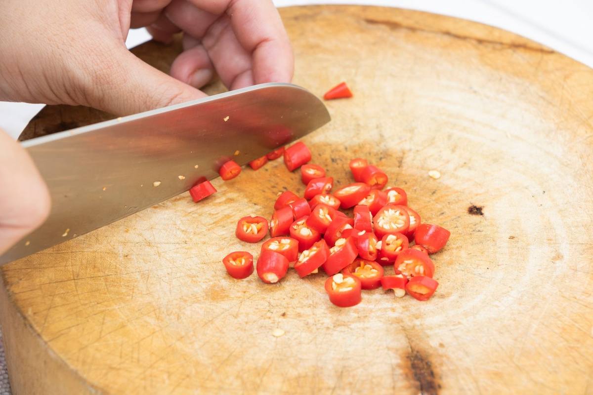 main coupant des piments rouges sur une planche à découper avec un couteau