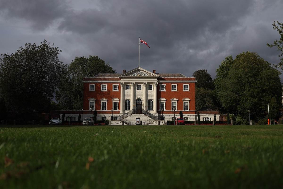 Maison rouge blanche avec colonnes et escaliers, devant un ciel sombre, voiture et arbres