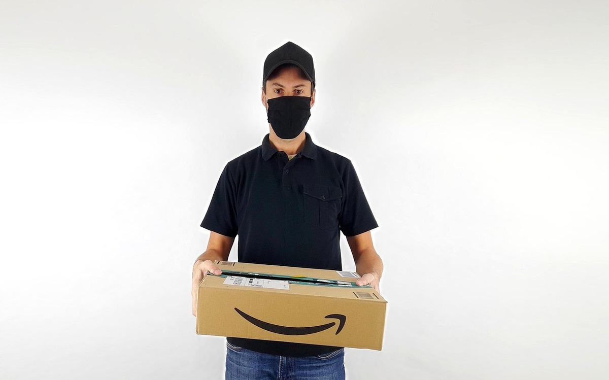 Personne en noir avec colis Amazon, visage masqué, contre fond neutre