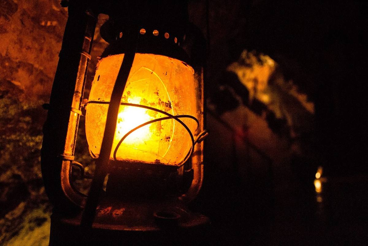 Lanterne à pétrole allumée suspendue la nuit, projetant une lumière chaude orangée sur les rochers environnants