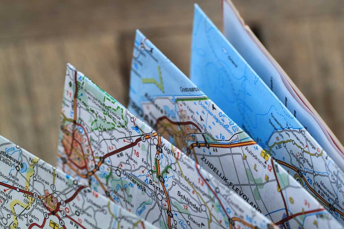 Plusieurs cartes routières pliées et dépliées, superposées sur une table