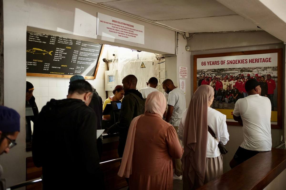 File d'attente dans un restaurant avec un menu visible, clients de diverses origines
