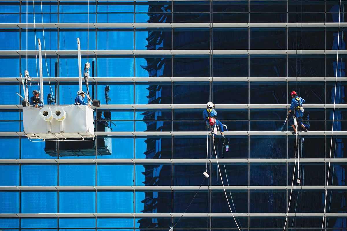 Travailleurs en harnais nettoient les vitres d'un gratte-ciel sous un ciel bleu Travailleurs en harnais nettoient les vitres d'un gratte-ciel sous un ciel bleu