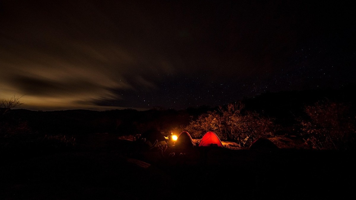 Campement de nuit en montagne avec tente rouge éclairée sous les étoiles