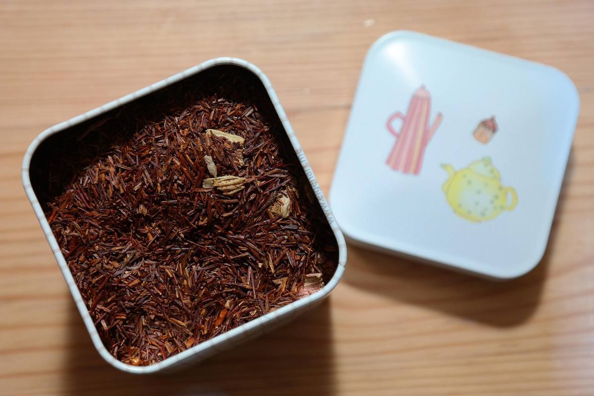 Boîte métallique contenant du rooibos, couvercle décoré, posé sur bois Boîte métallique contenant du rooibos, couvercle décoré, posé sur bois