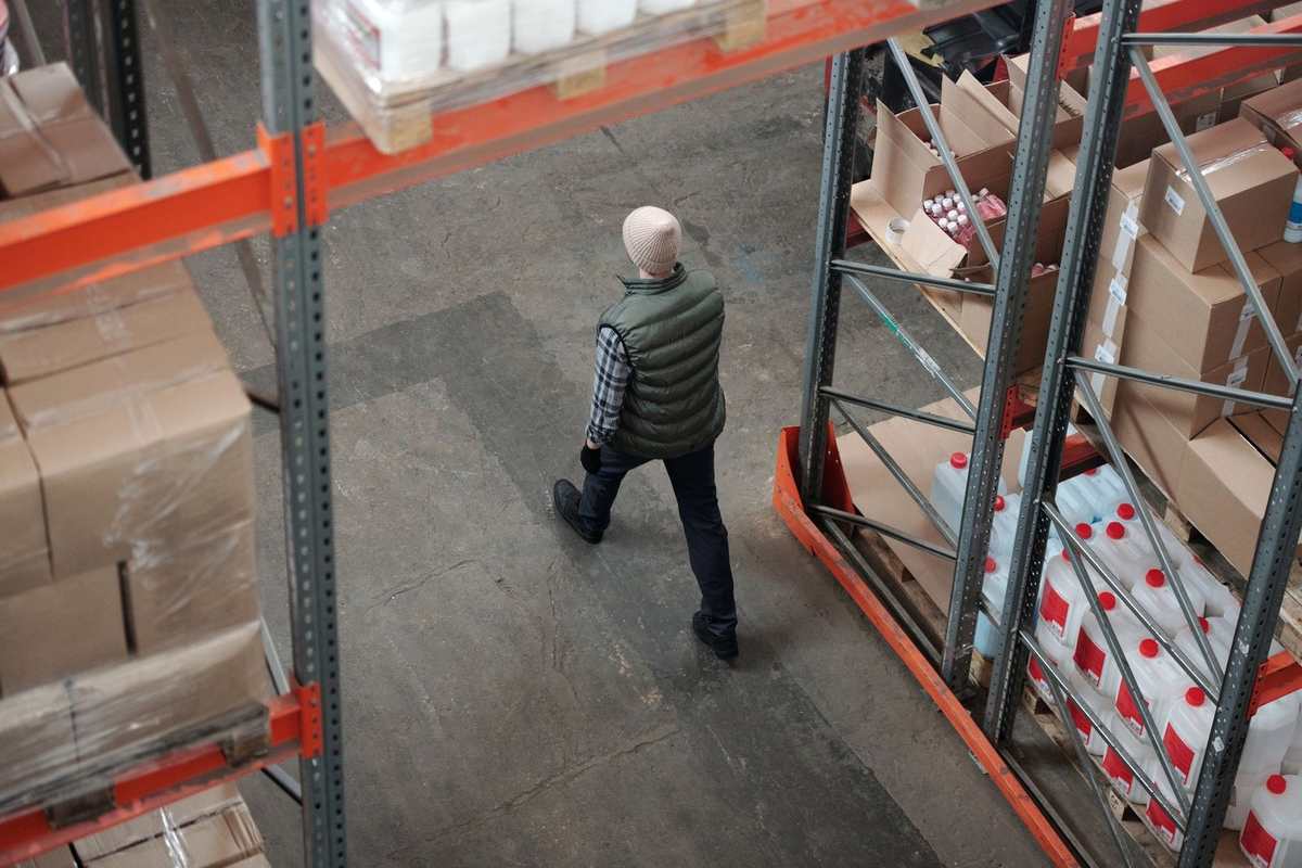 Homme en veston gris marche entre étagères orange chargées de boîtes dans un entrepôt