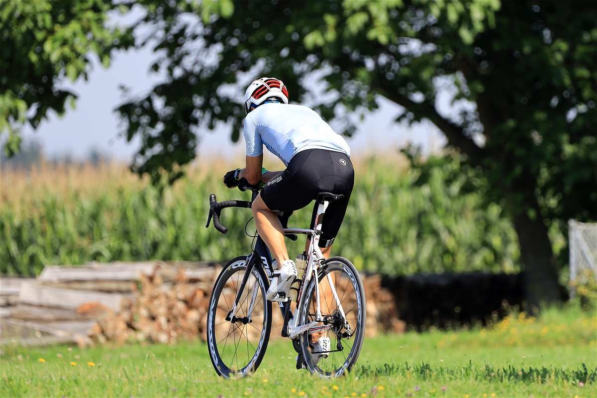 Cycliste en jersey blanc et short noir pédalant sur une route campagnarde avec champs et arbres Cycliste en jersey blanc et short noir pédalant sur une route campagnarde avec champs et arbres