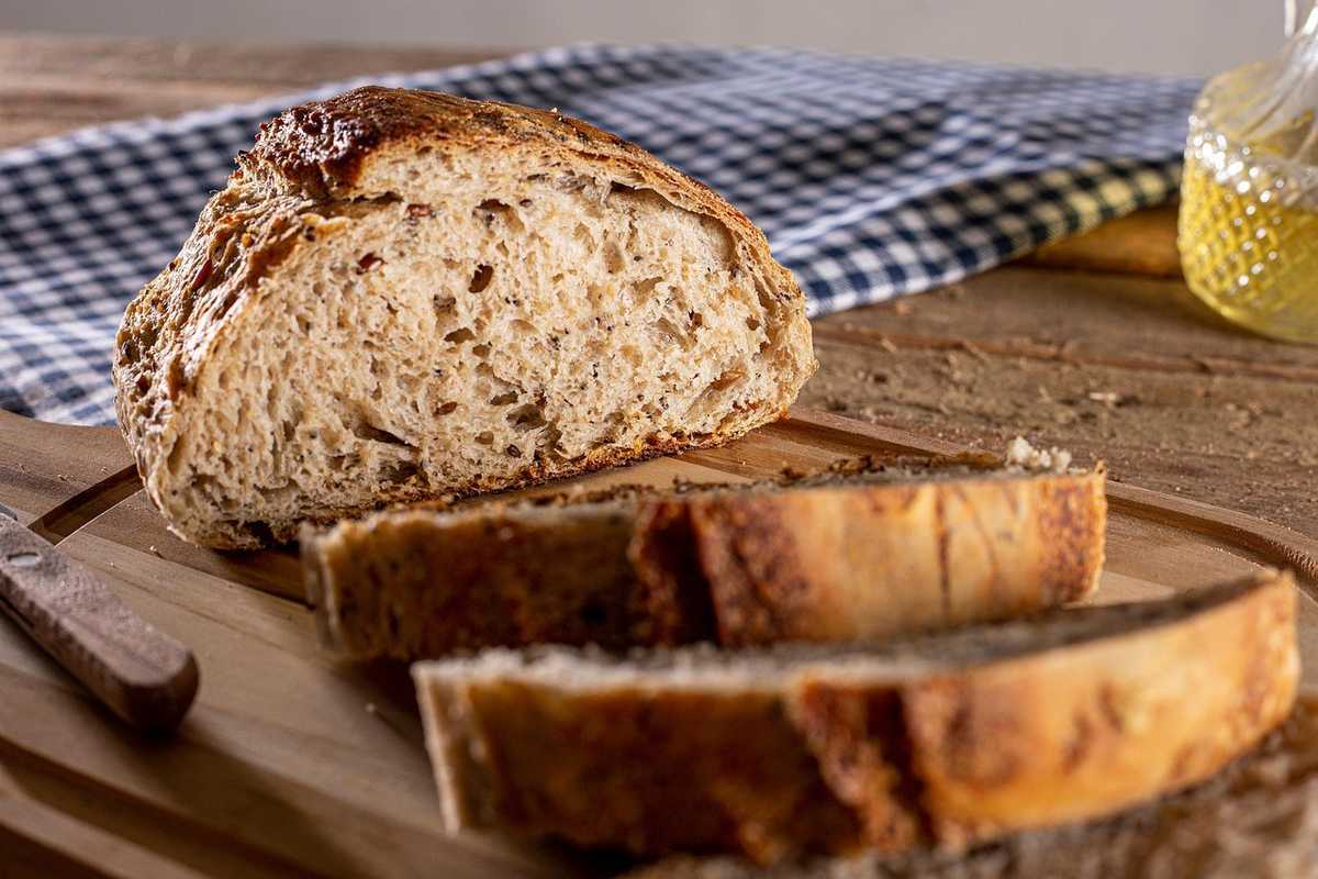 Pain de campagne rustique, tranches sur planche, couteau en bois, fond en bois et tissu à carreaux