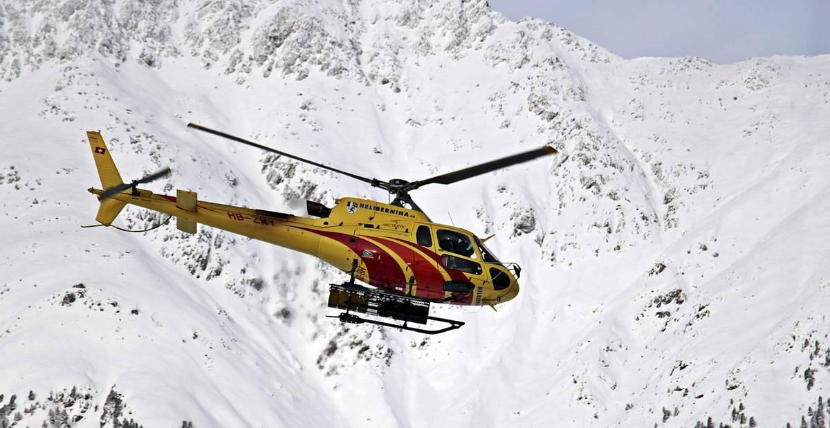 Un hélicoptère jaune et rouge vole au-dessus de montagnes recouvertes de neige Un hélicoptère jaune et rouge vole au-dessus de montagnes recouvertes de neige