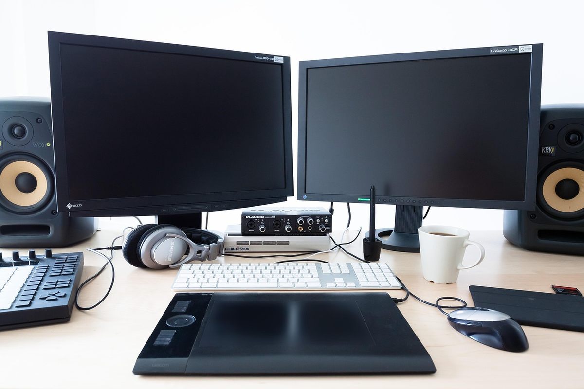 Bureau avec deux moniteurs noirs, ordinateur portable, claviers, souris et enceintes de monitoring