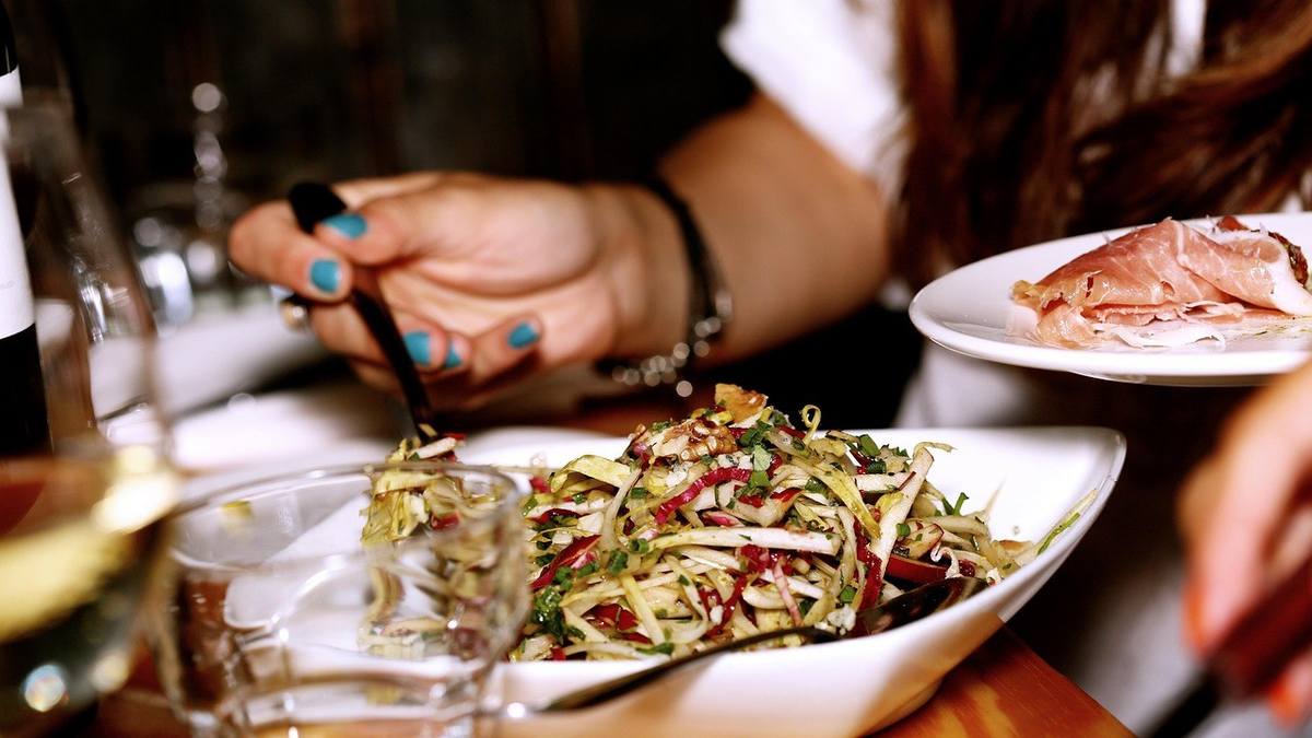 Femme mangeant une salade avec une fourchette, assiette blanche, verre de vin sur une table