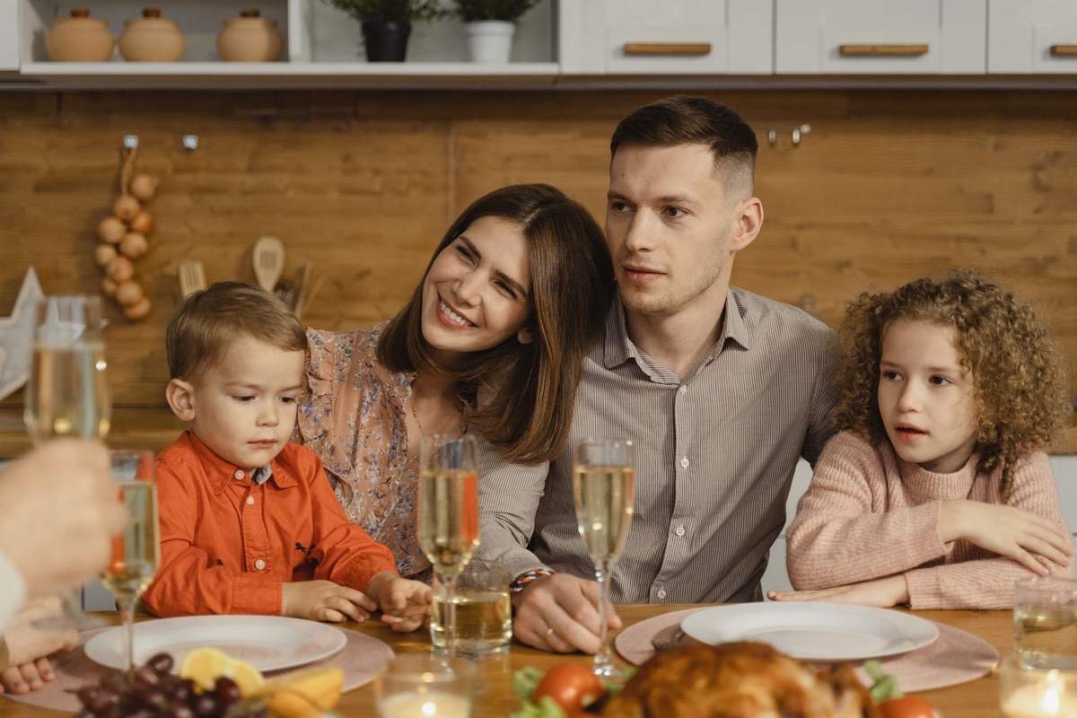 Famille en train de dîner dans une cuisine, avec verres, assiette, fruits et poulet sur la table Famille en train de dîner dans une cuisine, avec verres, assiette, fruits et poulet sur la table
