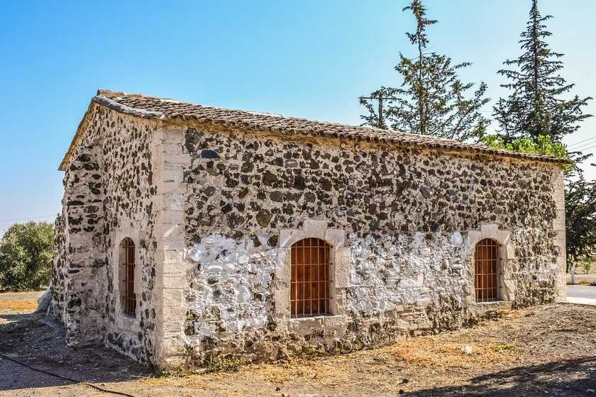 Maison en pierre sèche avec toiture en tuiles et fenêtres grillées, entourée de végétation sous un ciel bleu Maison en pierre sèche avec toiture en tuiles et fenêtres grillées, entourée de végétation sous un ciel bleu