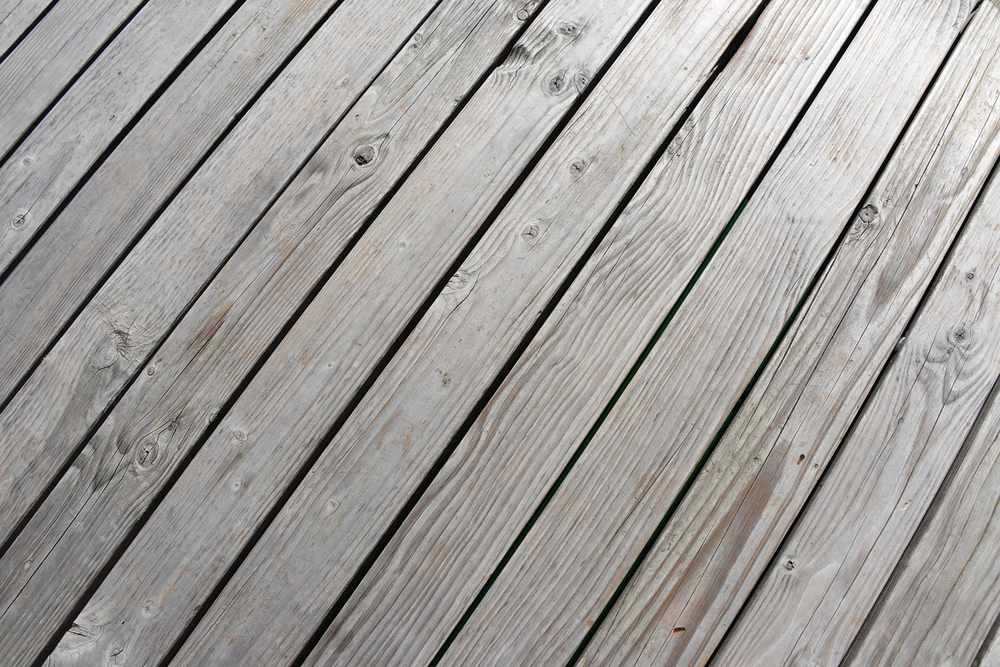 Planches de bois grises posées en diagonale sur un sol extérieur