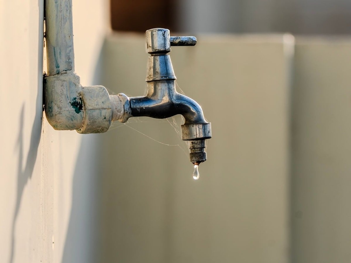 Un robinet fixé au mur laisse tomber une goutte d'eau