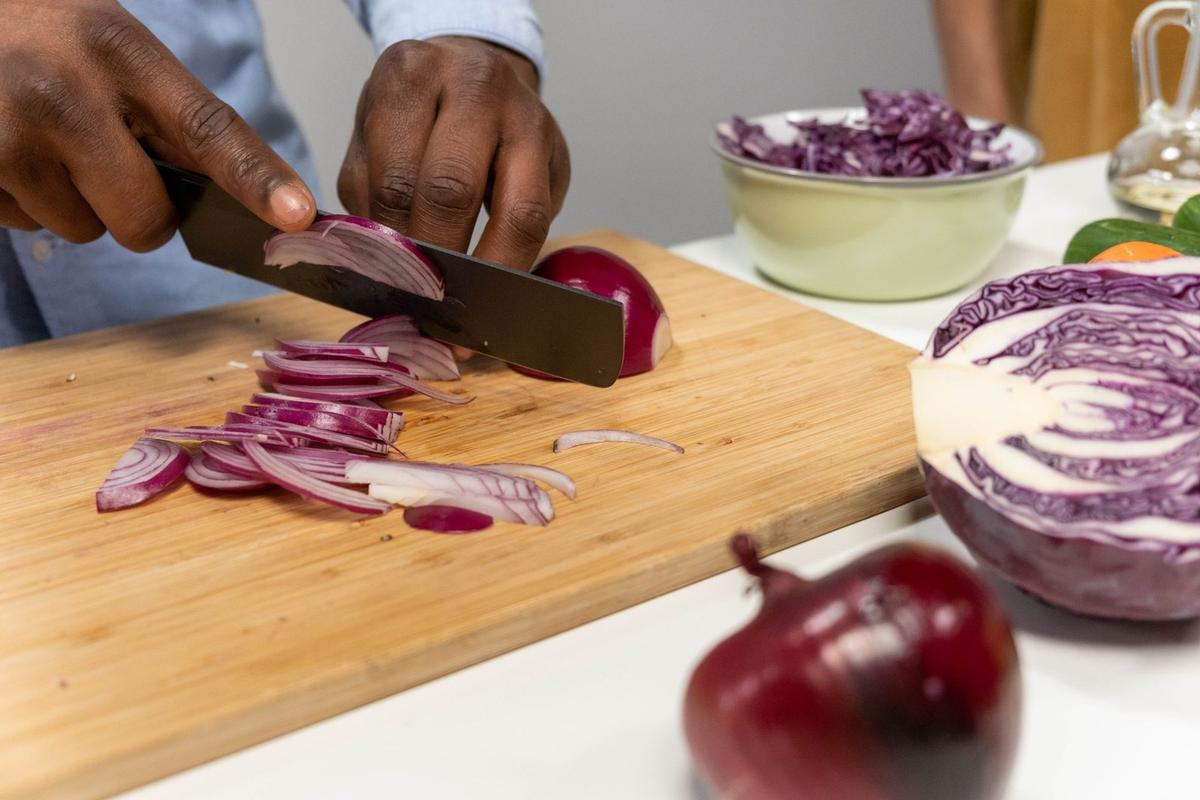 Personne tranchant des oignons rouges sur une planche à découper, légumes et bol à proximité